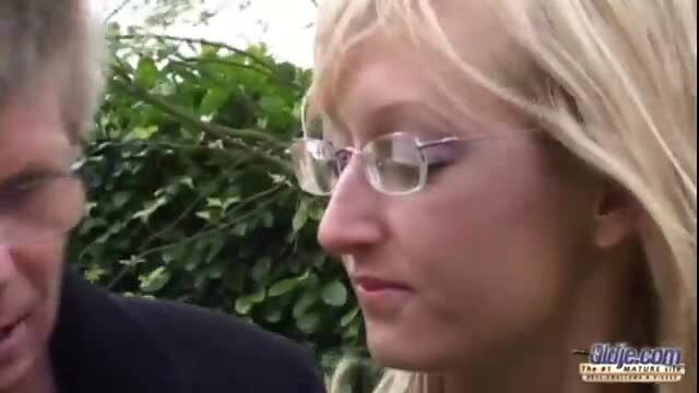 Blonde mature woman in glasses whispers intimately with older man outdoors