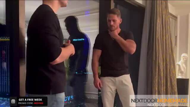 Two hot muscular guys in tight shirts chatting by window in hotel room service scene