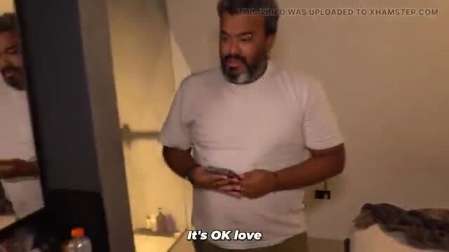 Busty mature Indian man in white tee holds belly by mirror in bedroom