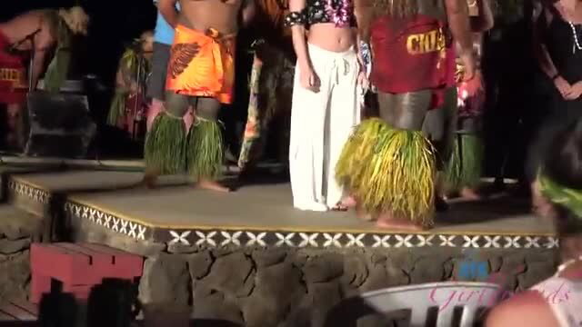 Polynesian hula dancers in grass skirts on outdoor stage, public exposure tease