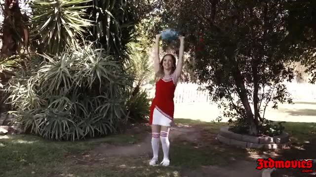 Cheerleader girl in red skirt and white stockings holds blue ball outdoors