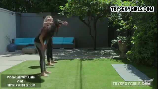 Blonde yoga teacher bends over with brunette student in sexy yoga session