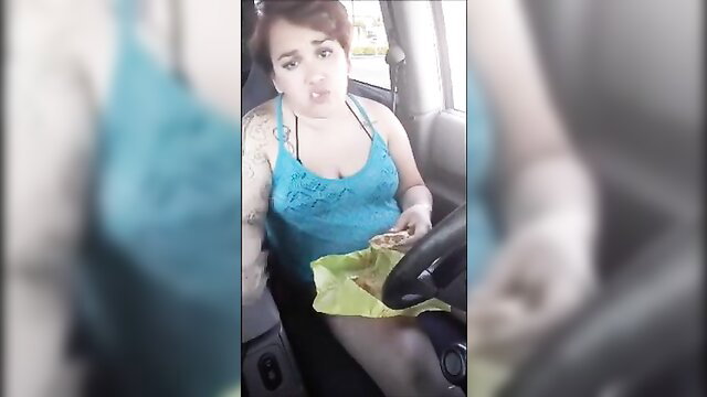Tattooed brunette in blue tank top eating kebab while driving car