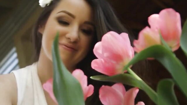 Cute Asian brunette in white top playfully nuzzling pink tulips closeup