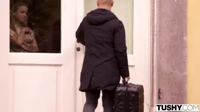 Bald man with suitcase greets sexy blonde through glass door