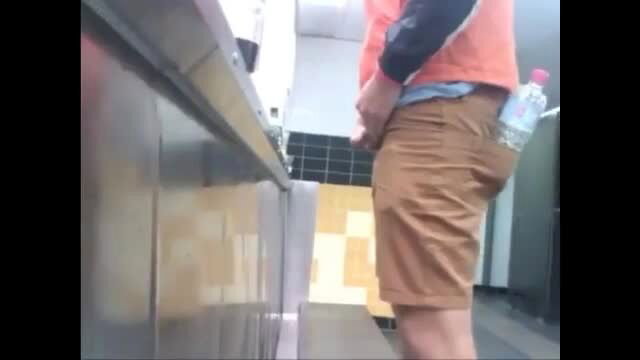 Guy peeing at urinal in shorts, bulge visible, public restroom voyeur