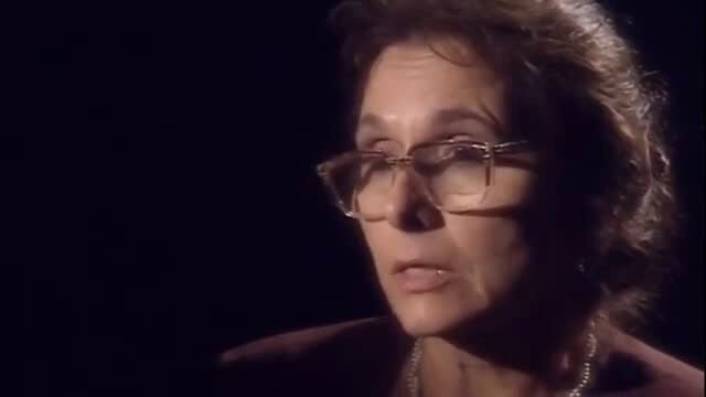 Mature brunette woman with glasses in dark interview-style closeup