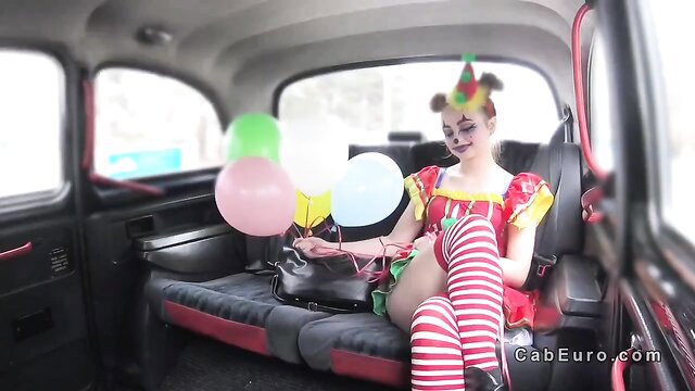 Blonde clown girl in sexy costume with balloons in fake taxi