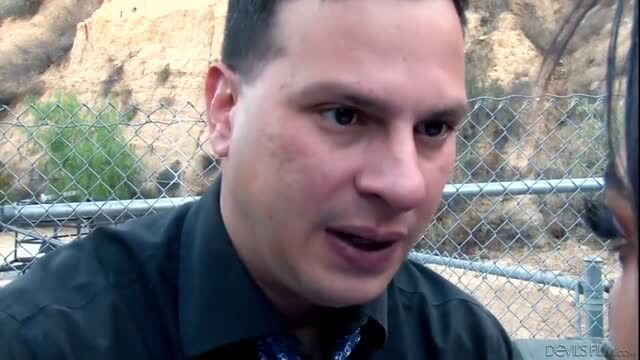 Maya Bijou talks passionately in outdoor interview, black shirt, chainlink fence backdrop