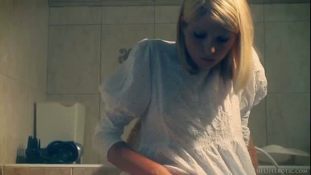 Blonde in sheer white dress lifts skirt in bathroom, teasing upskirt view