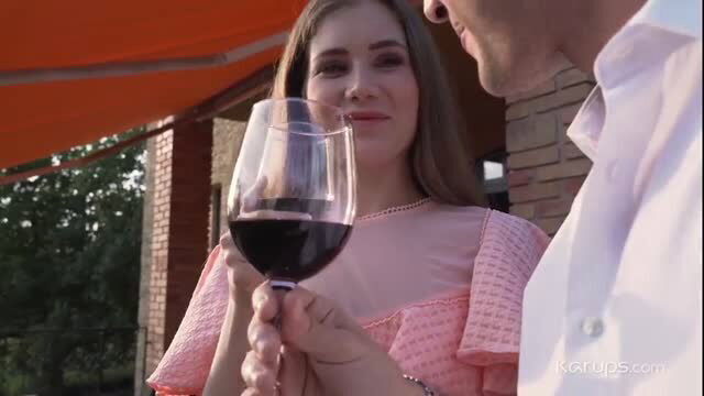 Mary Rock in sheer pink dress holds wine glass smiling at man outdoors
