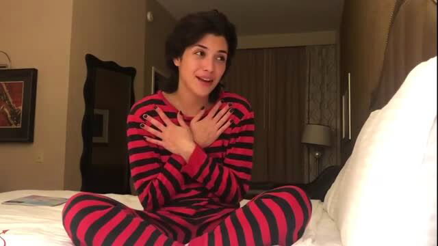 Curvy brunette in red black striped pajamas on bed, excited expression