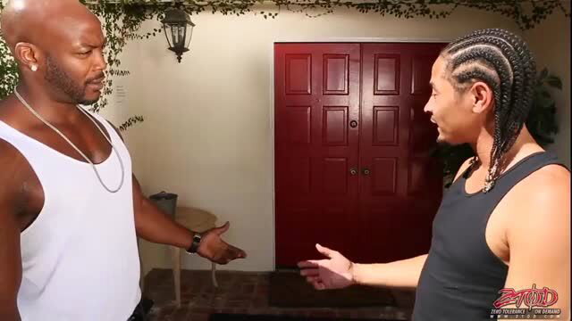 Two muscular black men with dreads talking outside in tank tops