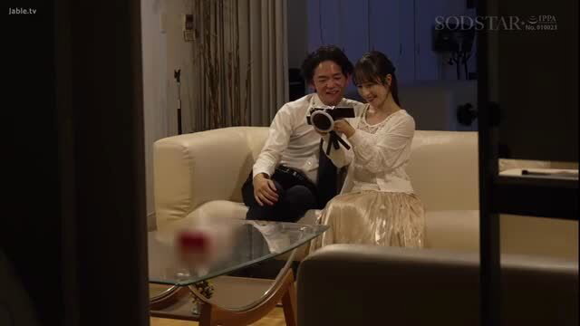 Japanese JAV couple on sofa, man photographing smiling woman in blouse skirt