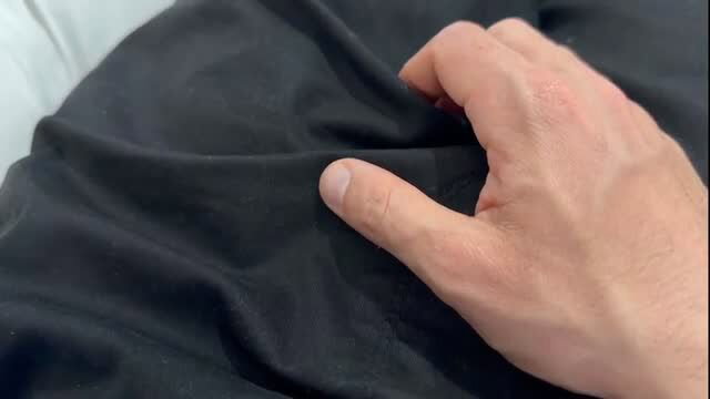 Man's hand gripping black fabric on bed, teasing closeup view