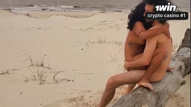 Nude couple embraces intimately on sunny beach log