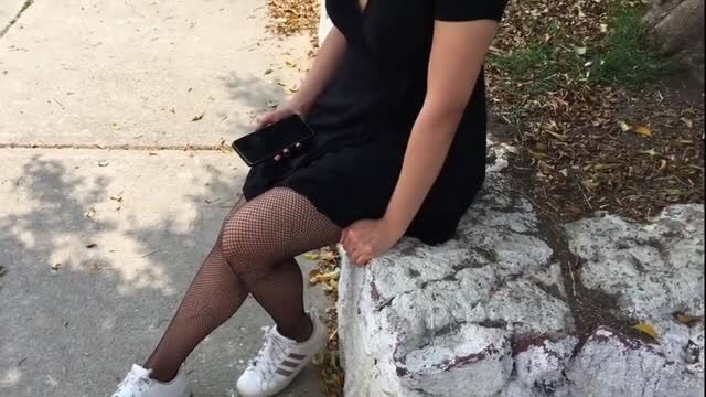 Hot Latina in black mini dress and fishnet stockings sits on wall, teasing legs