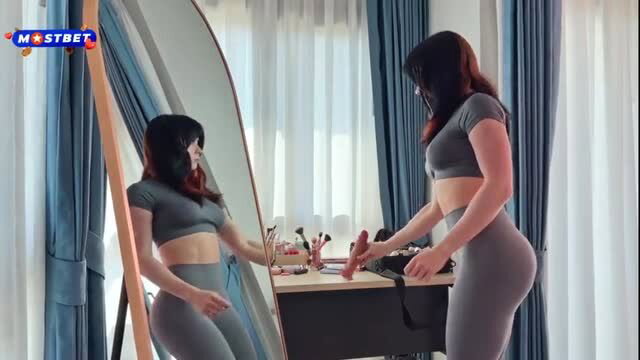 Sweetie Fox in tight gray leggings and crop top, posing by mirror