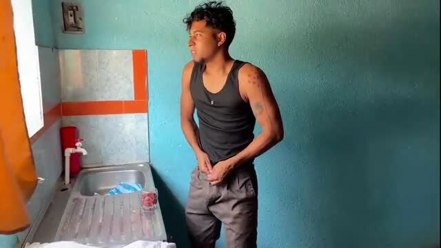 Tattooed Latino guy in tank top and pants in kitchen, amateur hookup vibe