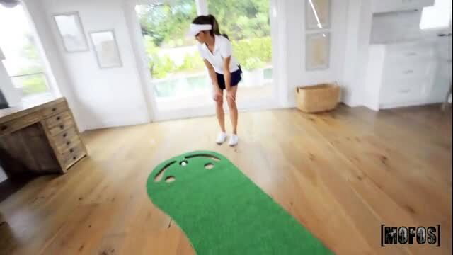 Asian golfer babe in short skirt bends over putting green indoor