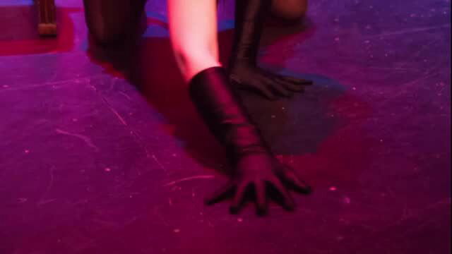 Closeup of pale woman's sexy black latex gloved hand on purple lit stage