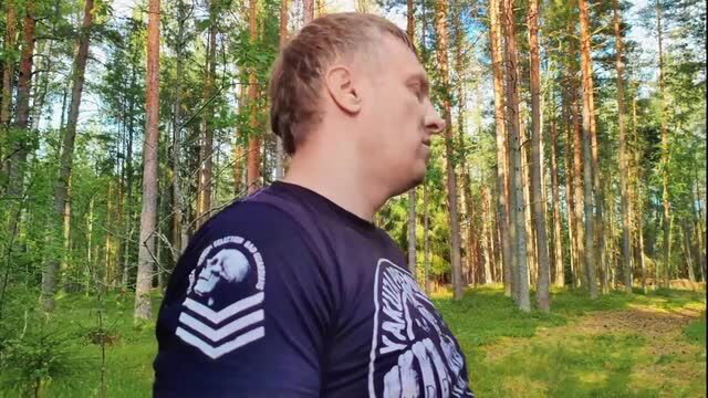Bald muscular guy in skull shirt standing in sunny woods forest