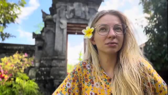 Blonde woman in yellow floral dress and frangipani flower at Bali temple gate