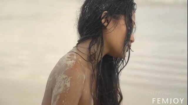 Black haired Asian beauty poses nude with wet sandy skin by sea