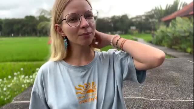 Blonde AI girlfriend in glasses and loose tee poses outdoors in Bali rice fields