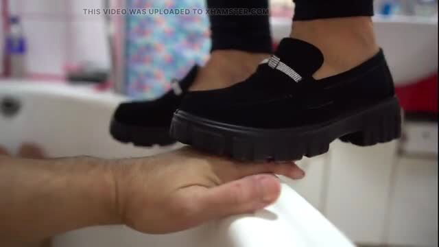Crush model steps on man's hand in bathtub with black platform loafers
