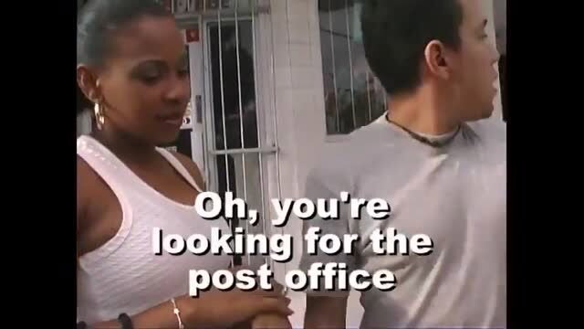 Preggo black woman in white tank top talks to Asian guy outside post office