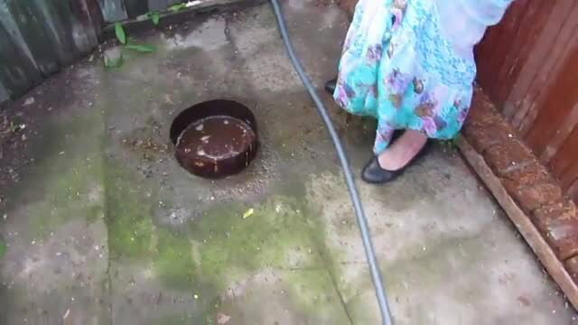 Mature woman in floral dress peeing outdoors into drain