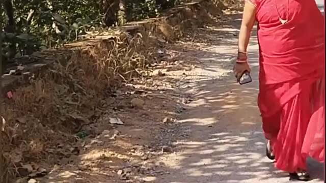 Desi woman in red sari walking on rural forest path holding phone