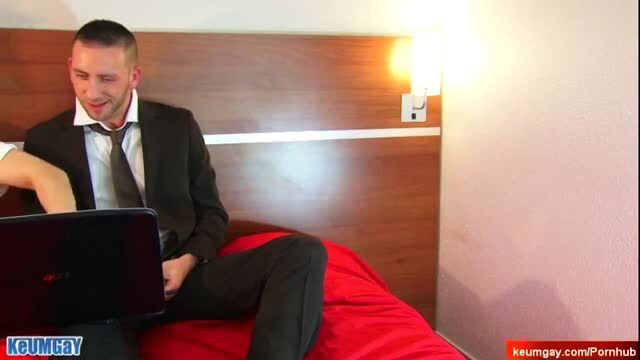 Suited man gets oral service on bed in gay porn scene