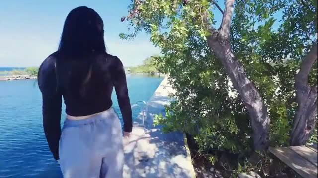Woman in sheer black top walking by water on outdoor path