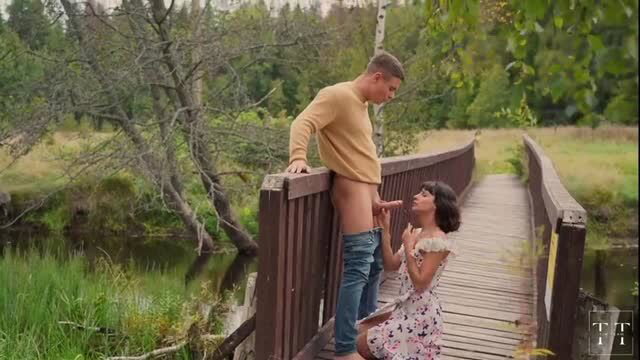 Brunette kneels giving outdoor blowjob on bridge