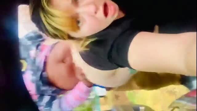 Woman in black top exposing breast while holding baby in bed selfie