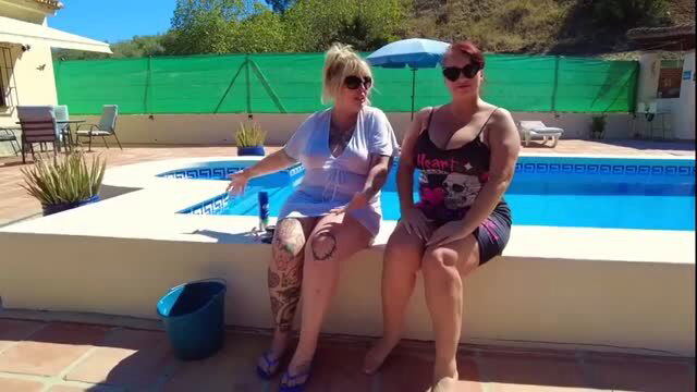 Two thick women sitting poolside in swimsuits, one with extensive leg tattoos