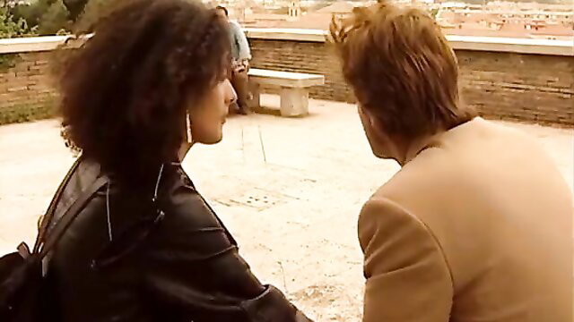 Curly-haired black woman in leather jacket chats with redhead man on terrace in Tinto Brass erotic short
