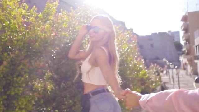 Blonde mature babe in crop top and jeans holds hand on sunny vacation stroll