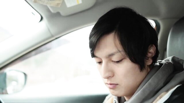 Handsome young Japanese man in hoodie sits pensively in car, JAV thumbnail