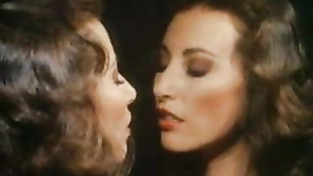 Two busty brunettes with big 80s hair in close-up face kiss