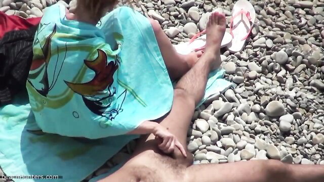 Hairy guy masturbating on pebbly beach near woman's flip-flops
