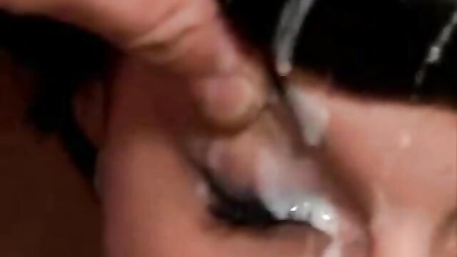 Closeup of woman with black bangs getting facial cumshot on eye