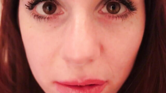 Closeup of seductive redhead woman with big eyes and glossy lips in ASMR mouth sounds video