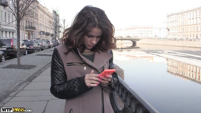 Emma Brown checking phone by river in sexy leather jacket
