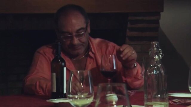 Bald man in red shirt sips wine at candlelit dinner table