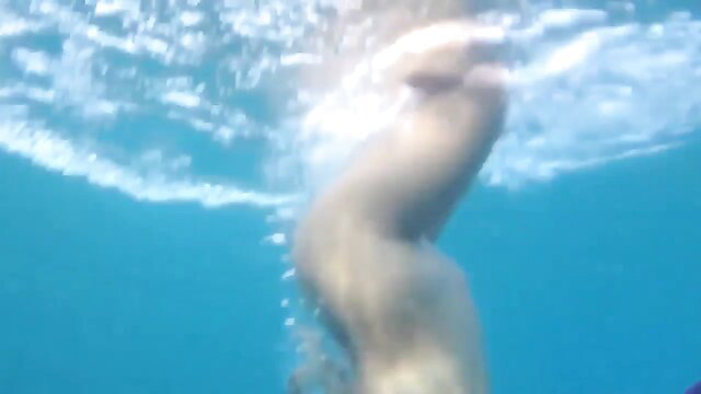 Blurry underwater closeup of nude woman's legs and ass swimming
