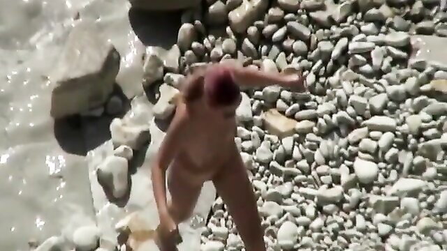 Nude woman with red hair running naked on sunny rocky beach