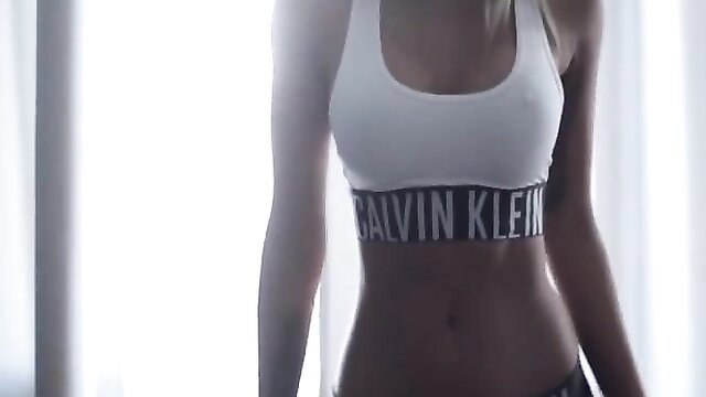 Slim Asian model in white Calvin Klein sports bra showing toned abs